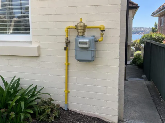 Yellow gas meter and pipework mounted on a painted brick exterior wall with a side path in Freshwater